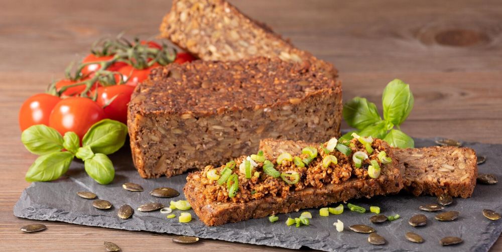 Vollkornbrot aufgeschnitten auf einer Steinplatte mit Tomaten, Kürbiskernen  und Basilikum dekoriert