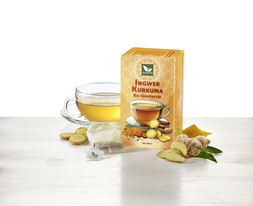 Tasse mit Tee davor beschriftete Verpackung und davor eine frische Ingwerwurzel auf einem Blatt